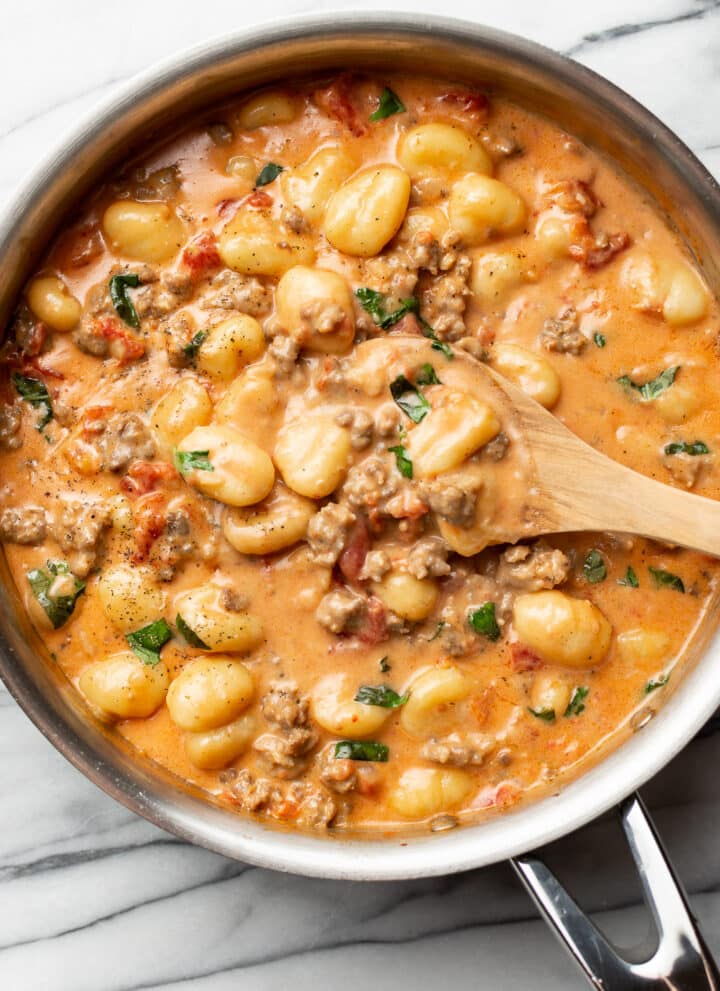 a skillet with italian sausage gnocchi and a wooden spoon