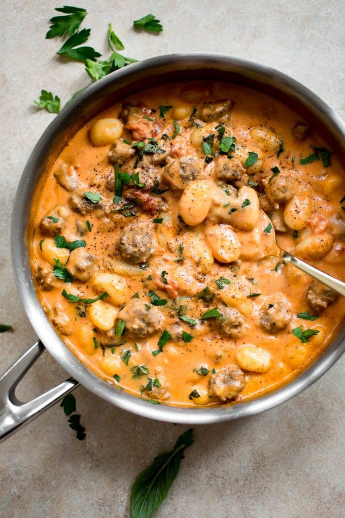 skillet with Italian sausage gnocchi and a serving spoon