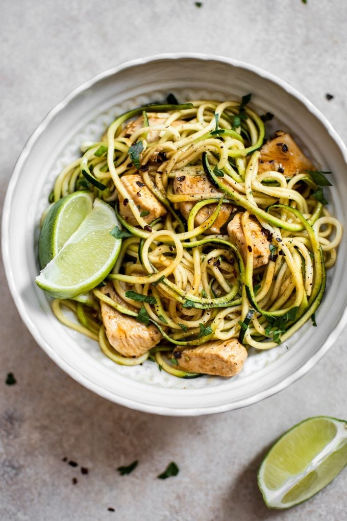 sweet and spicy chicken zoodles in a white bowl with lime