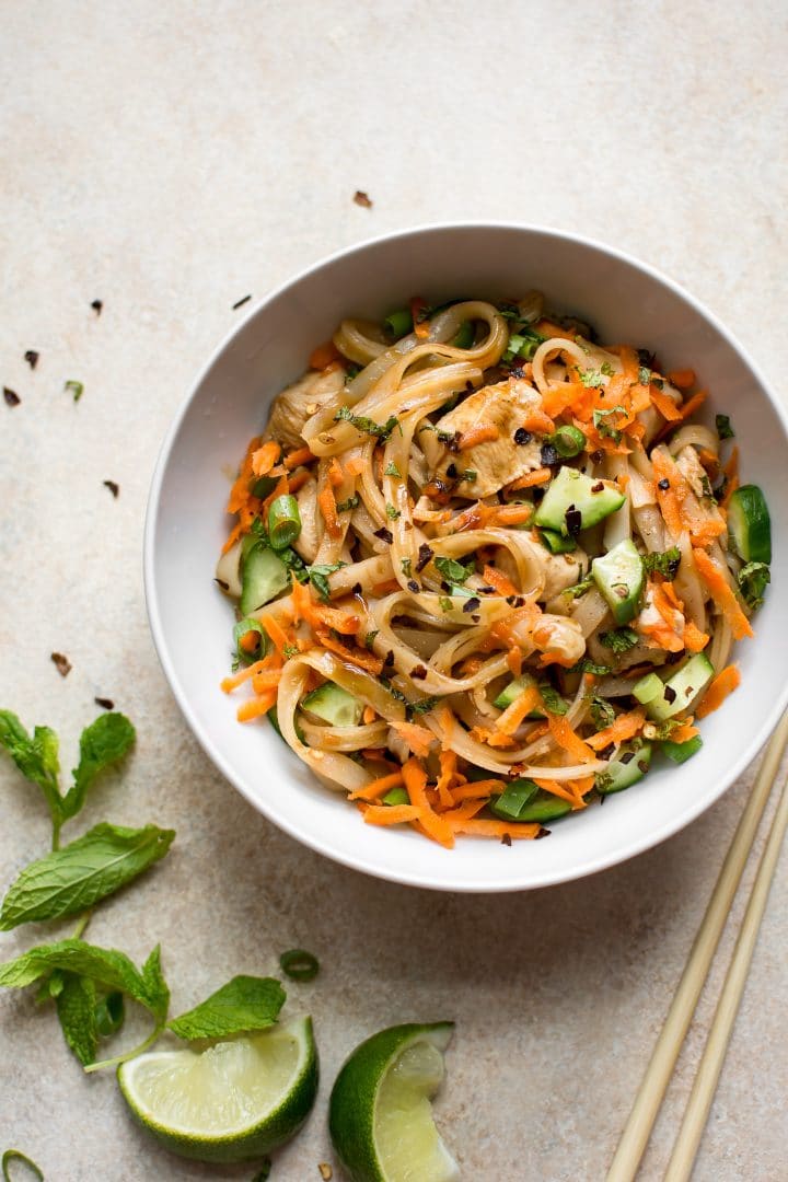 bowl of chicken rice noodle stir fry with lime, carrots, cucumber, and mint