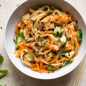 This healthy chicken stir fry with rice noodles is quick and delicious. Perfect for easy weeknight dinners! Garnished with scallions, mint, grated carrots, and cucumber.