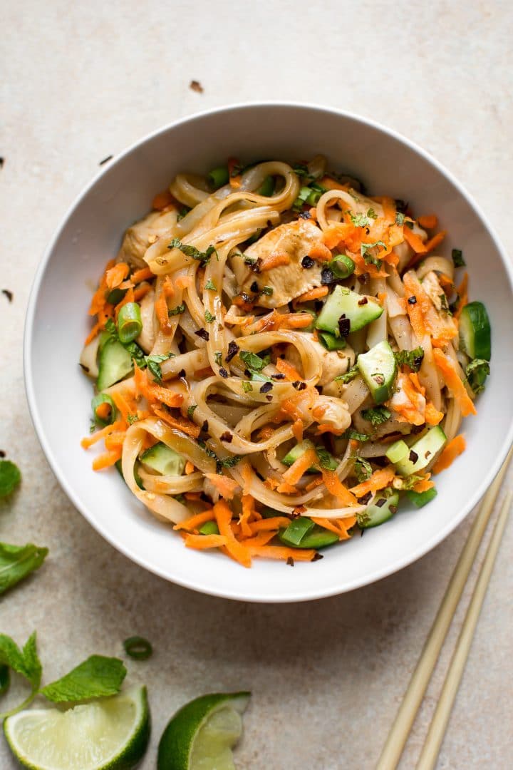 healthy chicken stir fry with rice noodles in a white bowl beside lime wedges and chopsticks