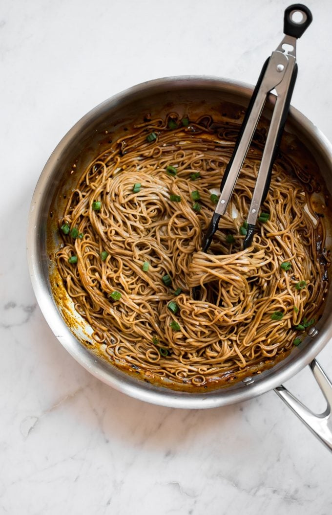 skillet with chili garlic noodles and tongs