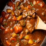 closeup of a slow cooker with beef stew and a wooden spoon
