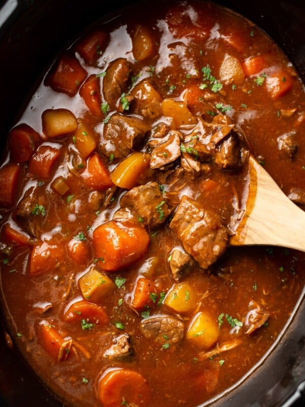 closeup of a slow cooker with beef stew and a wooden spoon