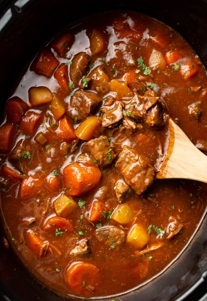 closeup of a slow cooker with beef stew and a wooden spoon