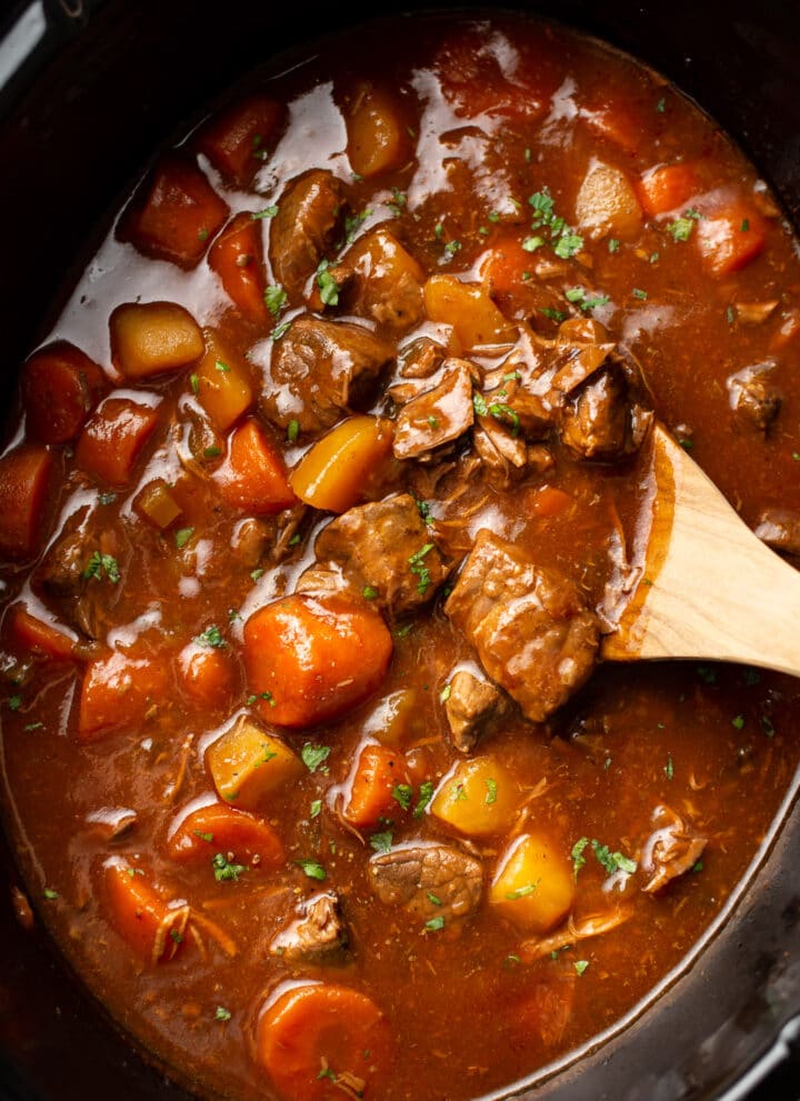 closeup of a slow cooker with beef stew and a wooden spoon