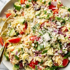 close-up of a bowl of mediterranean orzo salad with a serving spoon