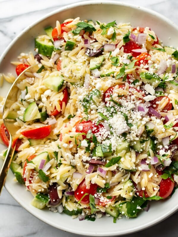 close-up of a bowl of mediterranean orzo salad with a serving spoon