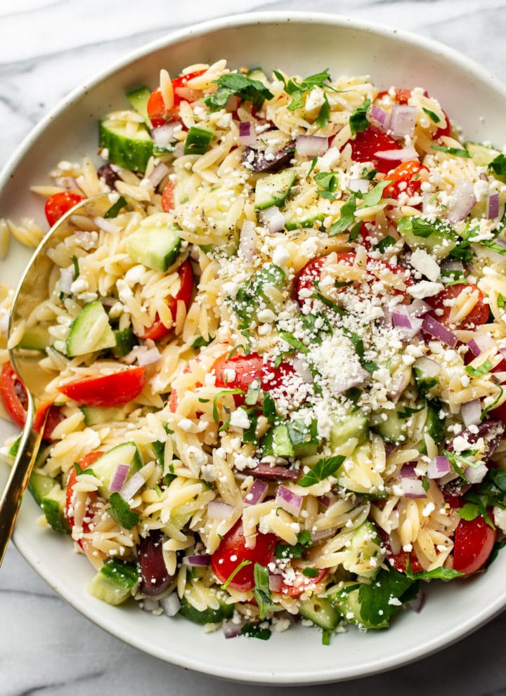 close-up of a bowl of mediterranean orzo salad with a serving spoon