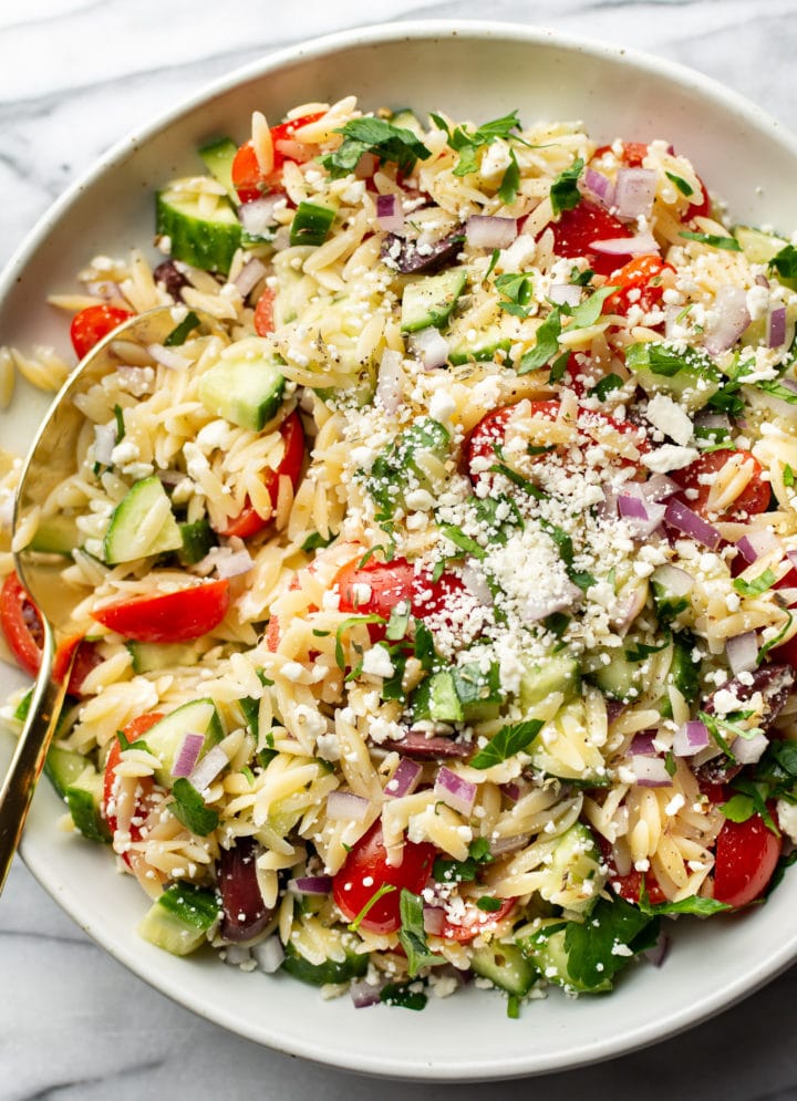 close-up of a bowl of mediterranean orzo salad with a serving spoon