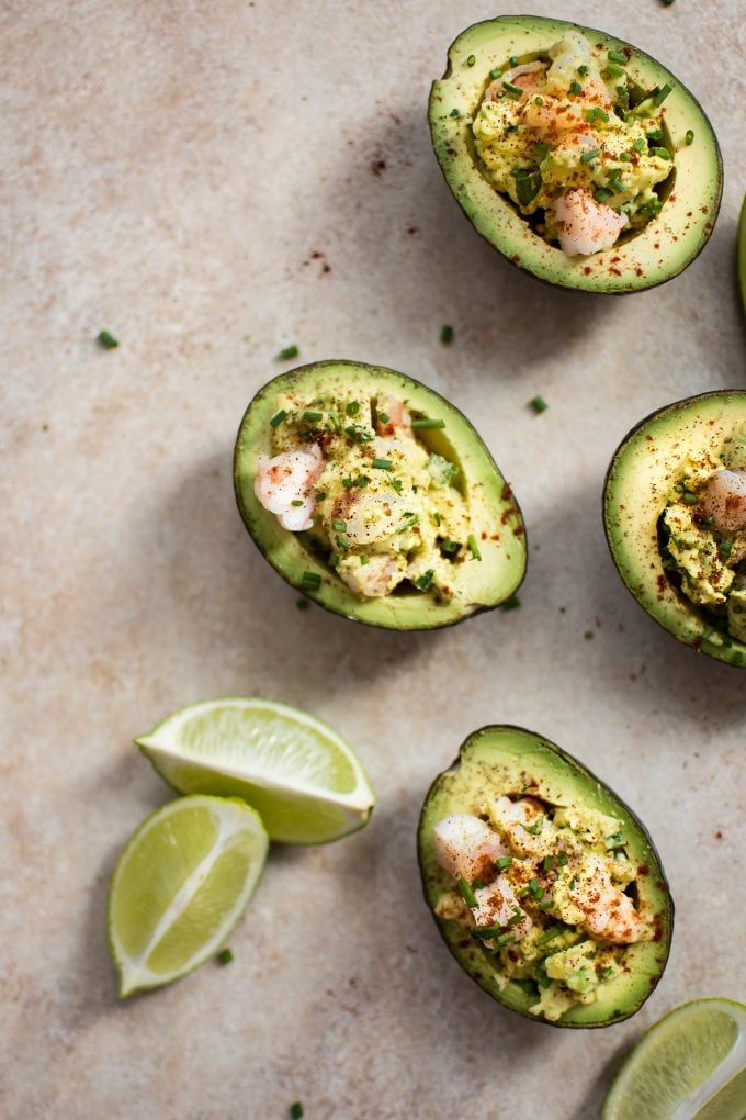 four shrimp stuffed avocado halves beside lime wedges