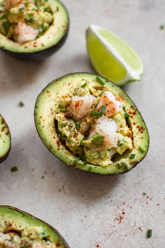 close-up of half an avocado stuffed with shrimp beside lime wedge