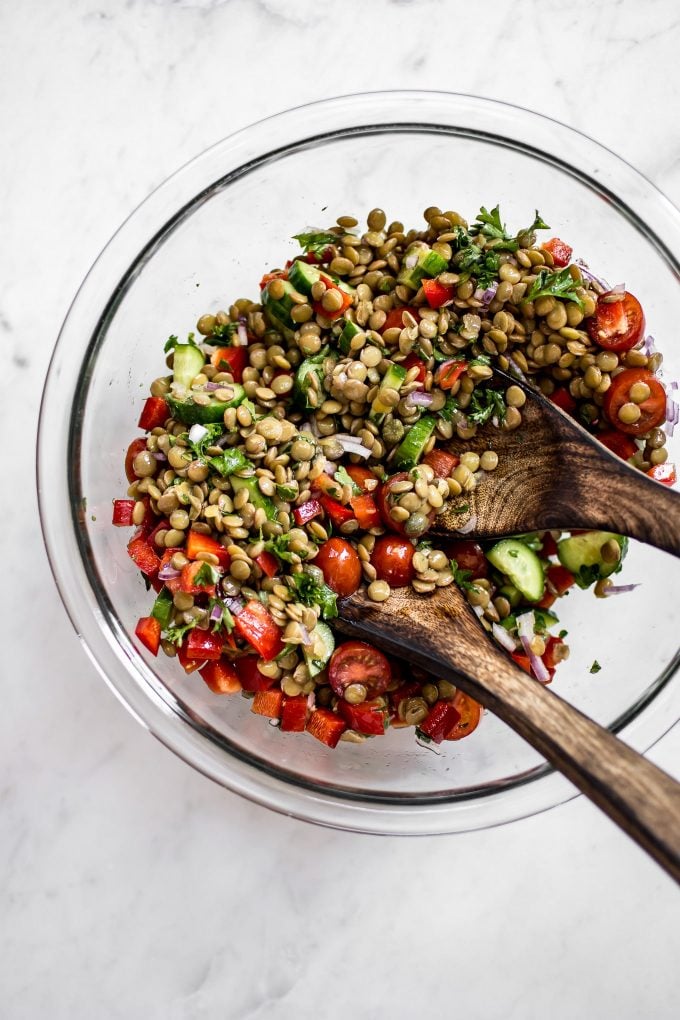 healthy lentil salad in a glass mixing bowl with salad utensils