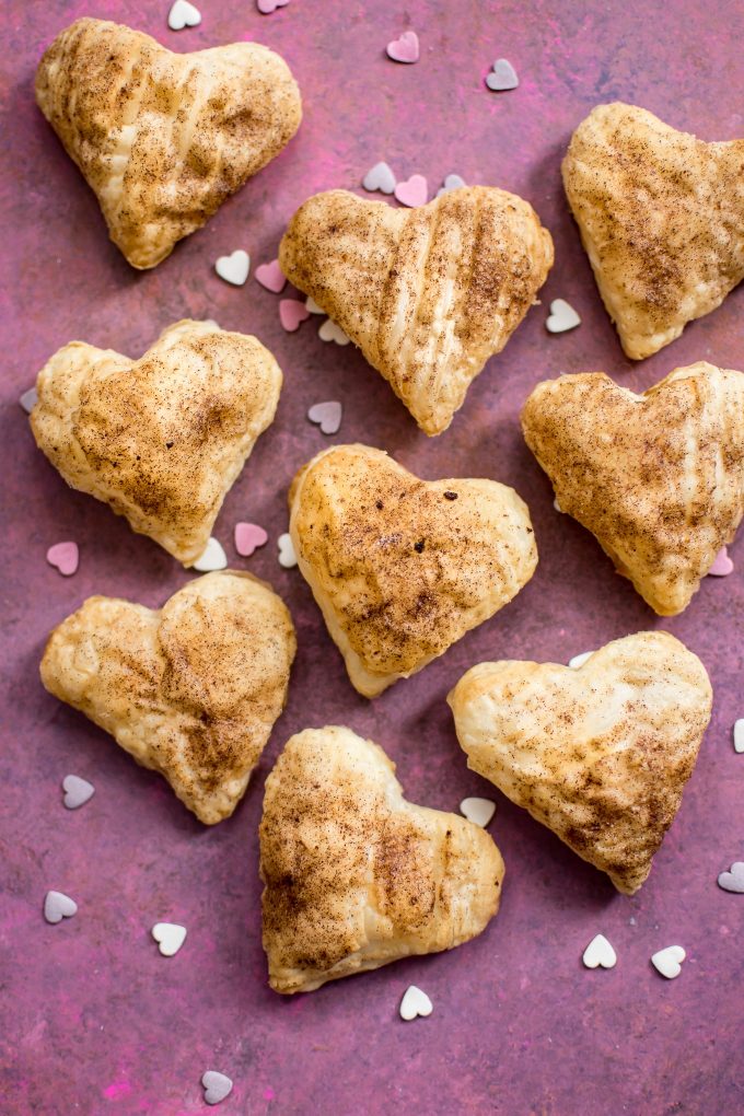 several heart-shaped puff pastries and heart sprinkles on purple surface