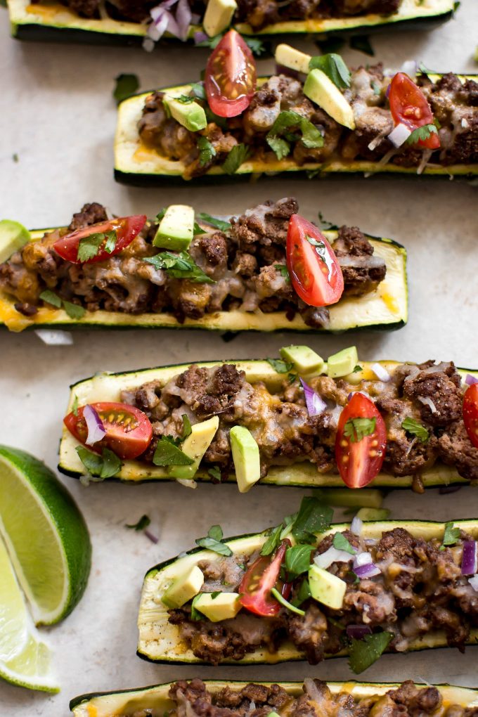 taco zucchini boats topped with ground beef, cheese, avocado, and tomatoes