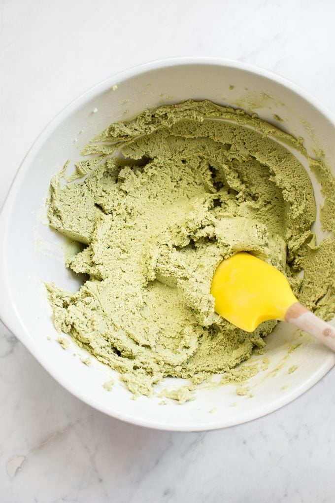 vegan matcha cookie batter in a white mixing bowl with a yellow spatula