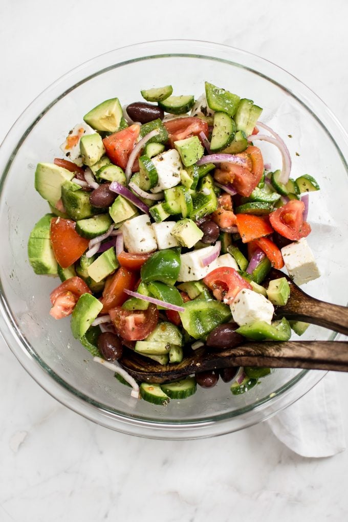 glass serving bowl with avocado Greek salad with tomatoes, feta, olives, and cucumber