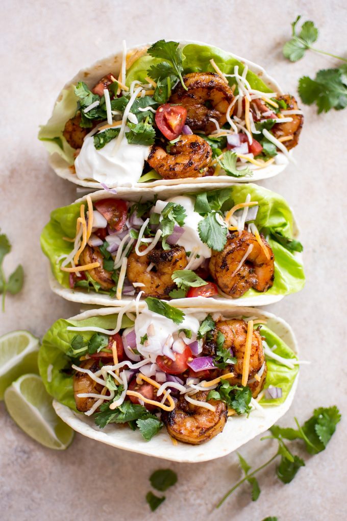 several blackened shrimp tacos with sour cream and lime wedges