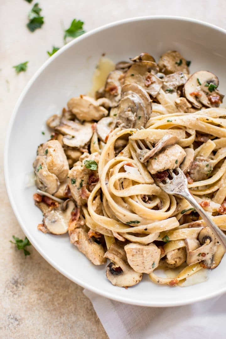 close-up of chicken bacon mushroom pasta on a white plate with a fork