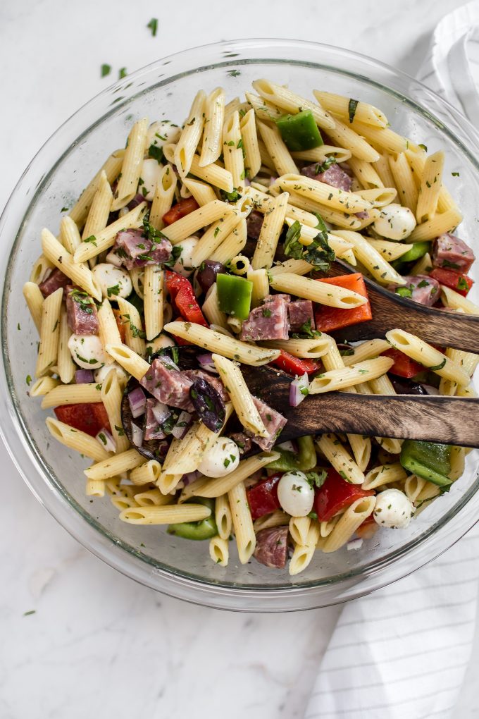 glass bowl with healthy Italian summer pasta salad and wooden serving utensils