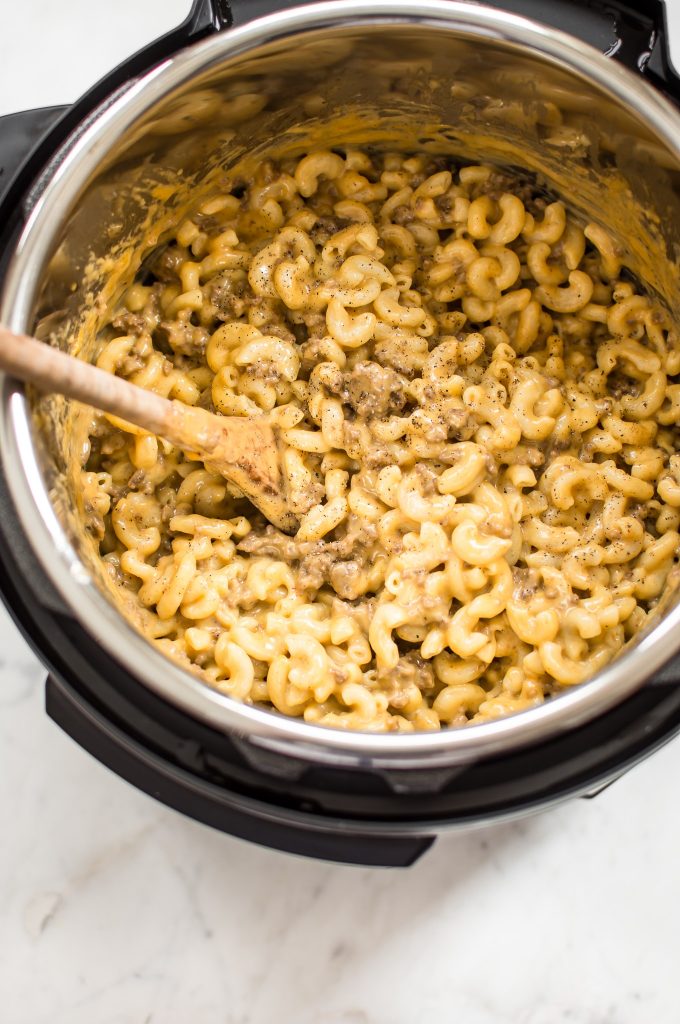 beef macaroni and cheese inside Instant Pot being stirred with wooden cooking spoon