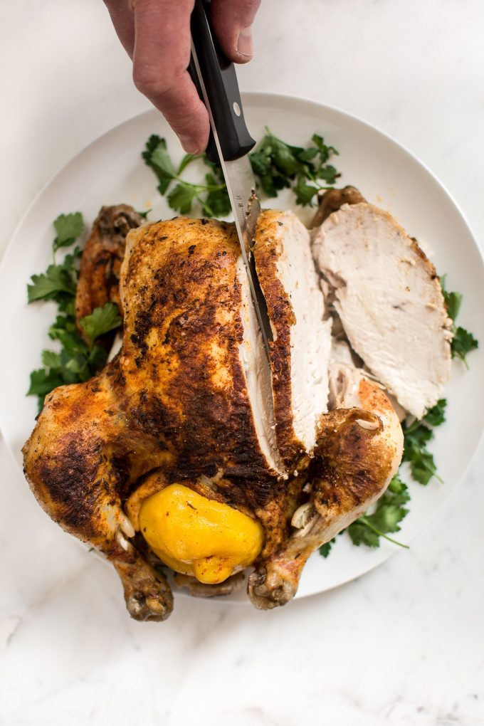 Instant Pot whole chicken on a white serving plate with a knife and parsley garnish