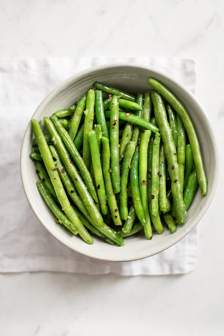 green beans with chili garlic butter in a bowl on a white cloth napkin