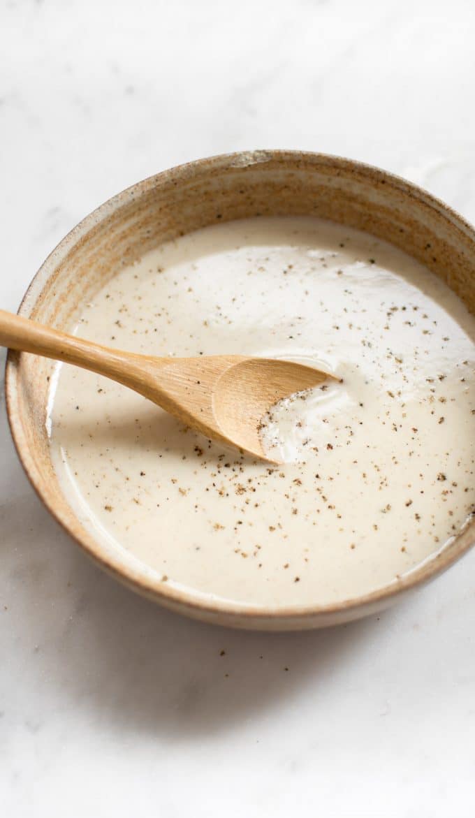 easy lemon tahini dressing in a stoneware bowl with a wooden cooking spoon