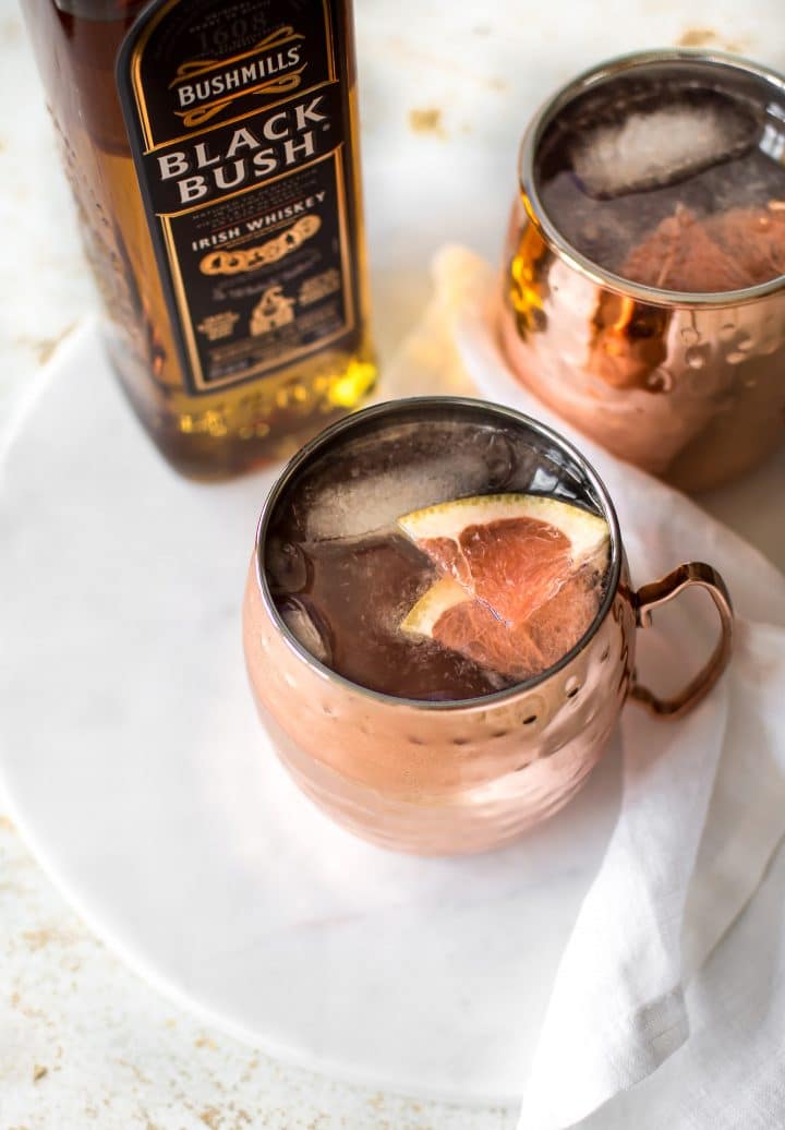 two mugs of grapefruit mule cocktail beside a bottle of Irish whiskey