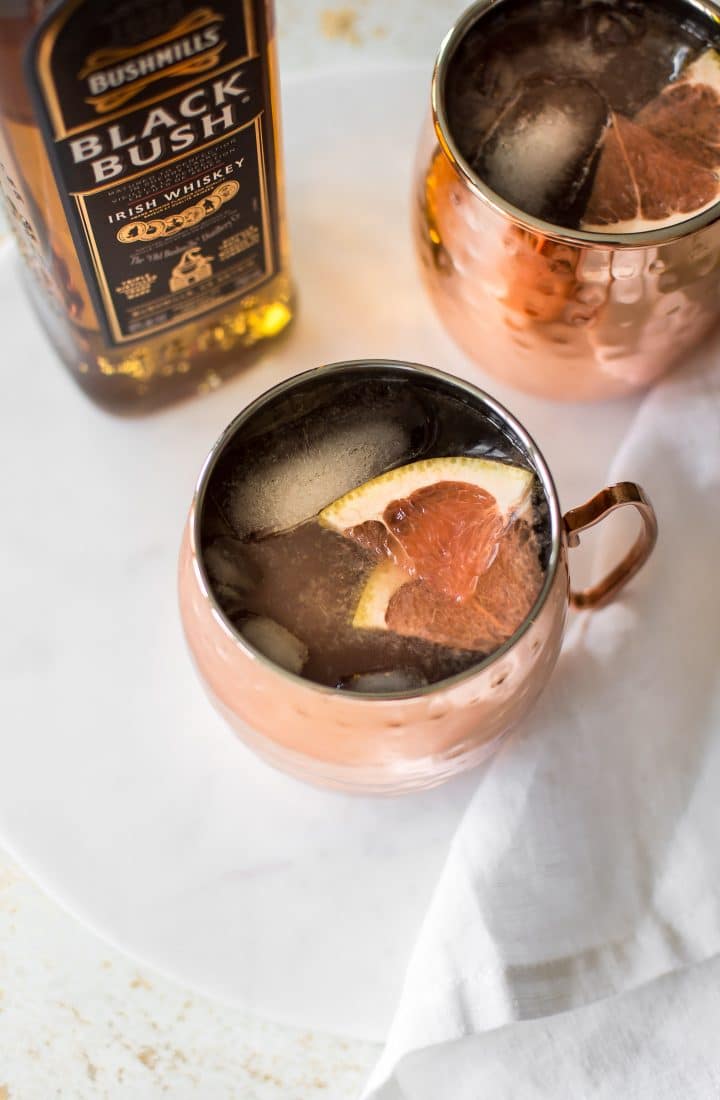 two grapefruit Irish mules in mugs with a bottle of whiskey