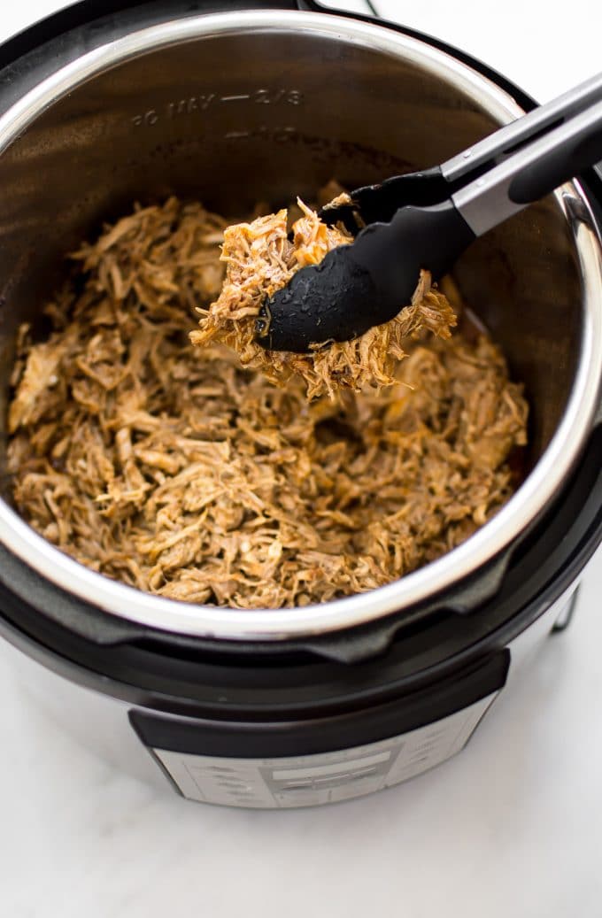 tender pulled pork and tongs in an Instant Pot