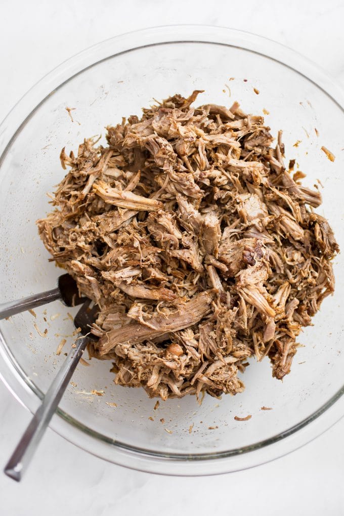 shredded pulled pork and two forks in a glass bowl