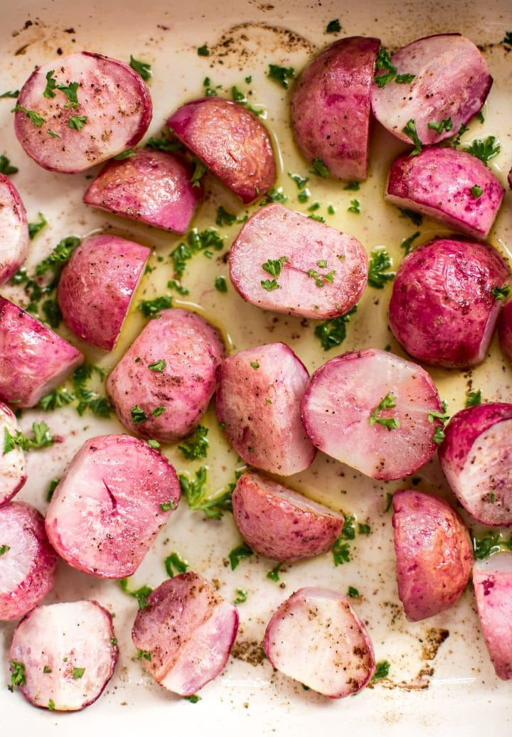 close-up of roasted vegan low-carb radishes in halves with olive oil, salt and pepper, and parsley garnish