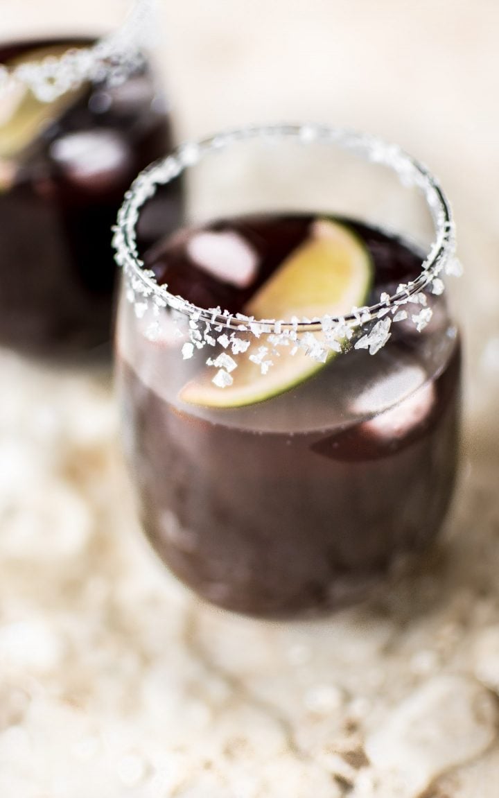 close-up of a black cherry margarita in a glass with a lime wedge and ice