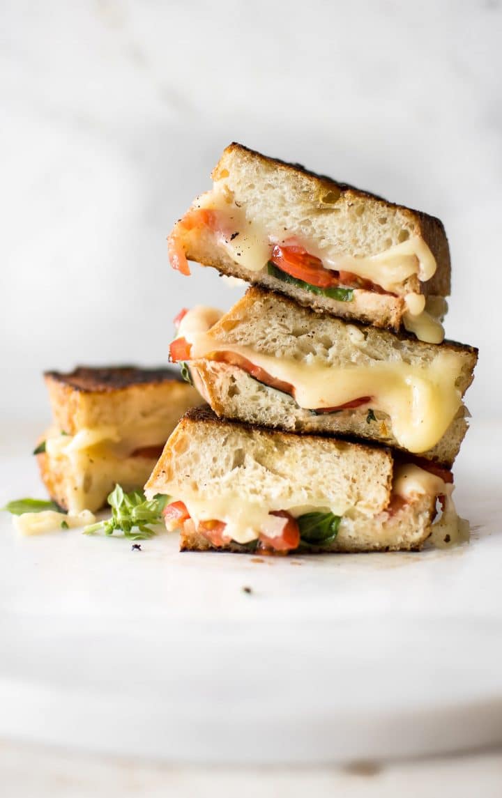 a stack of three vegetarian grilled cheese sandwiches with mozzarella, tomatoes, and basil