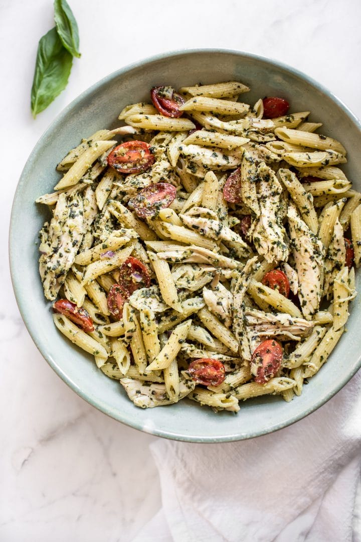 cold pesto pasta salad in a bowl beside basil leaf