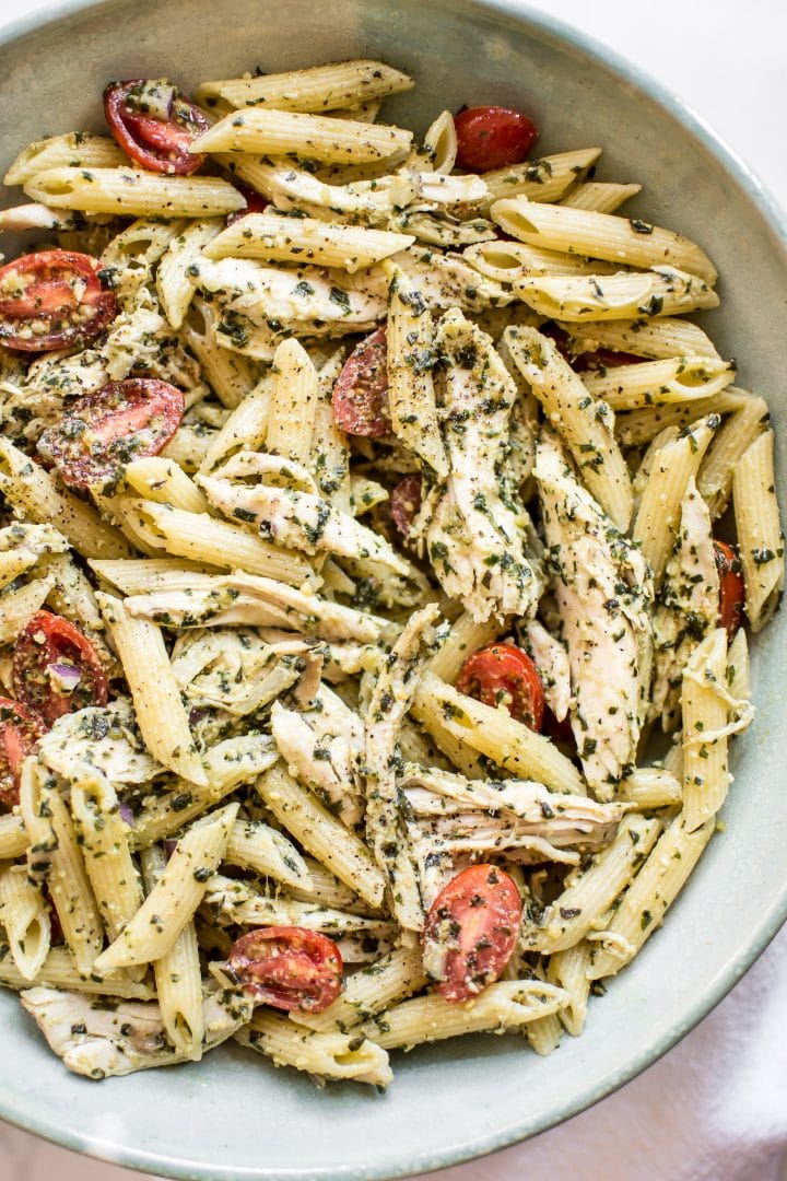 close-up of healthy cold pesto pasta salad with chicken, basil, and fresh tomatoes