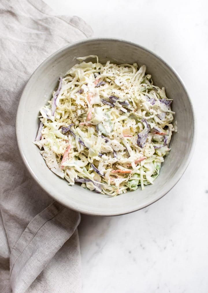 simple creamy coleslaw in a bowl beside a cloth tea towel