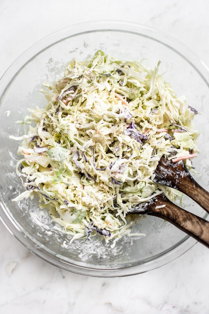 creamy coleslaw in a glass bowl with wooden salad utensils