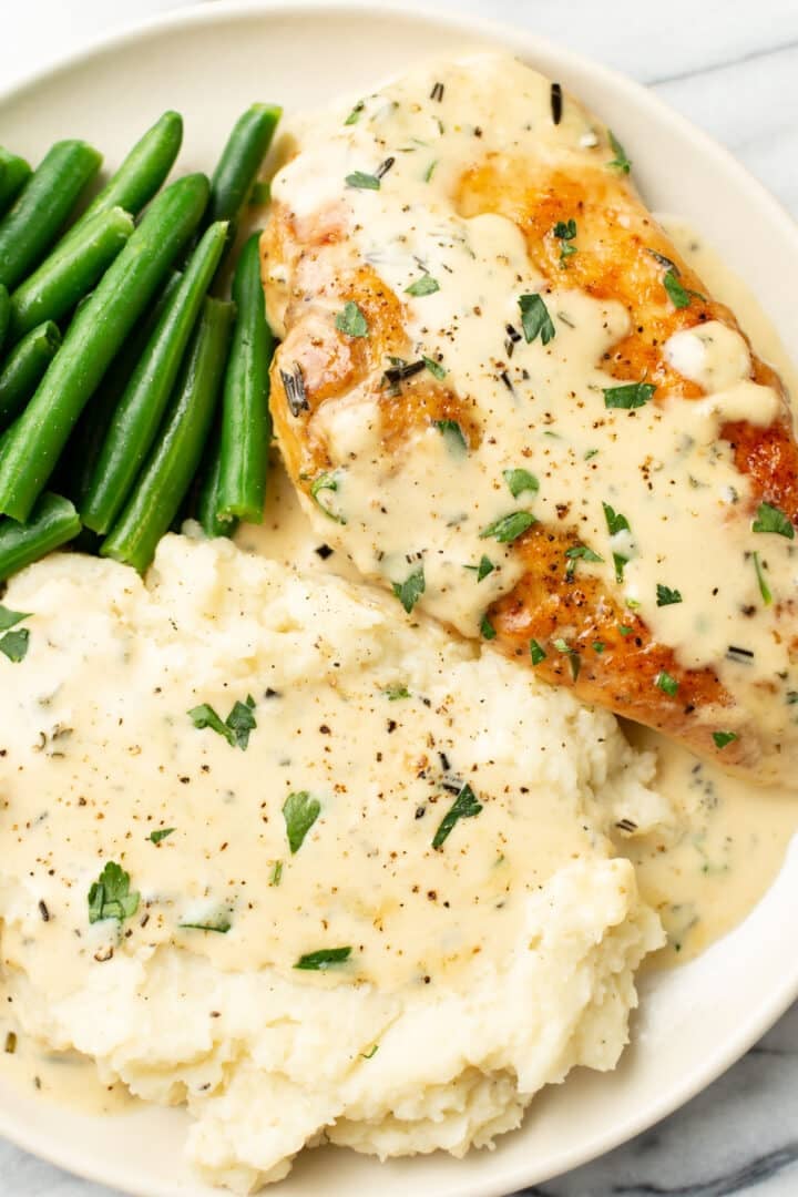 a plate with creamy herb chicken, green beans, and mashed potatoes