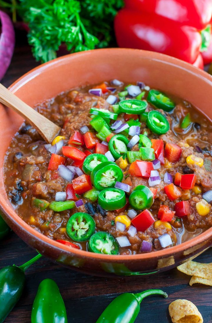vegan lentil chili in a bowl with a spoon and topped with sliced jalapenos