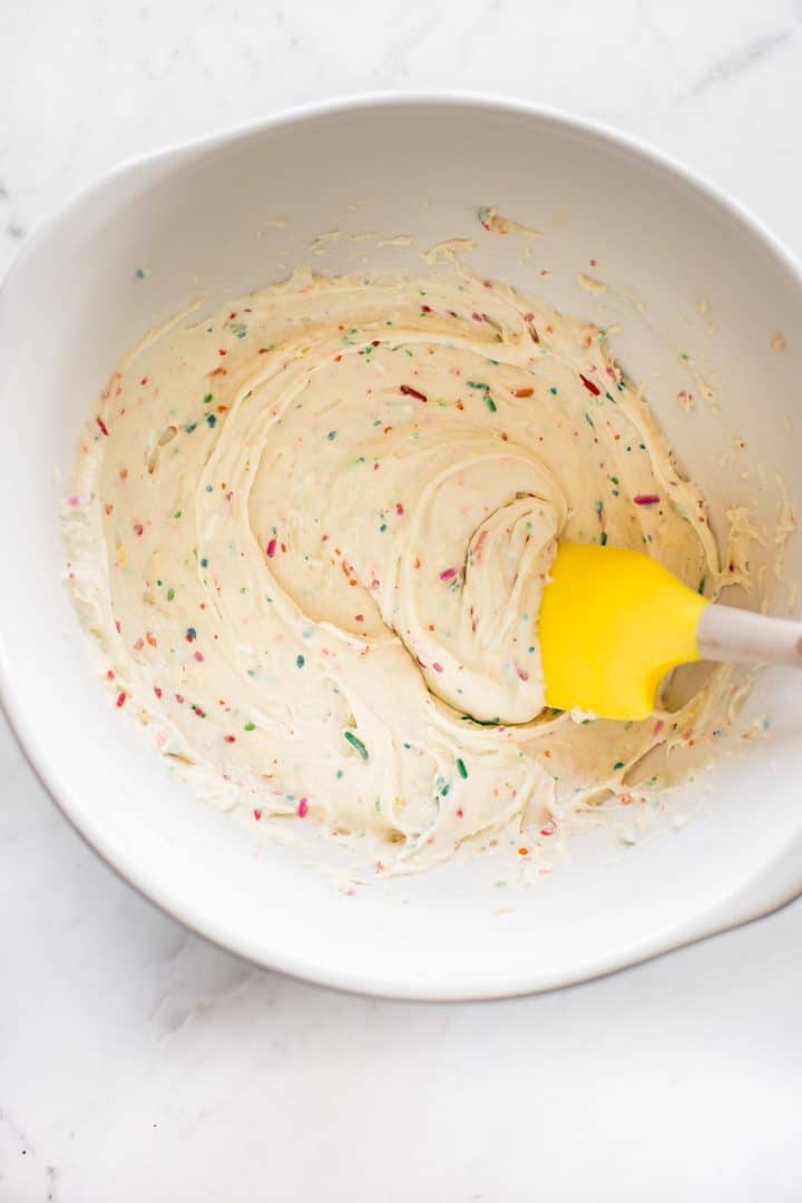  birthday sprinkles cookies batter in a white mixing bowl with a spatula