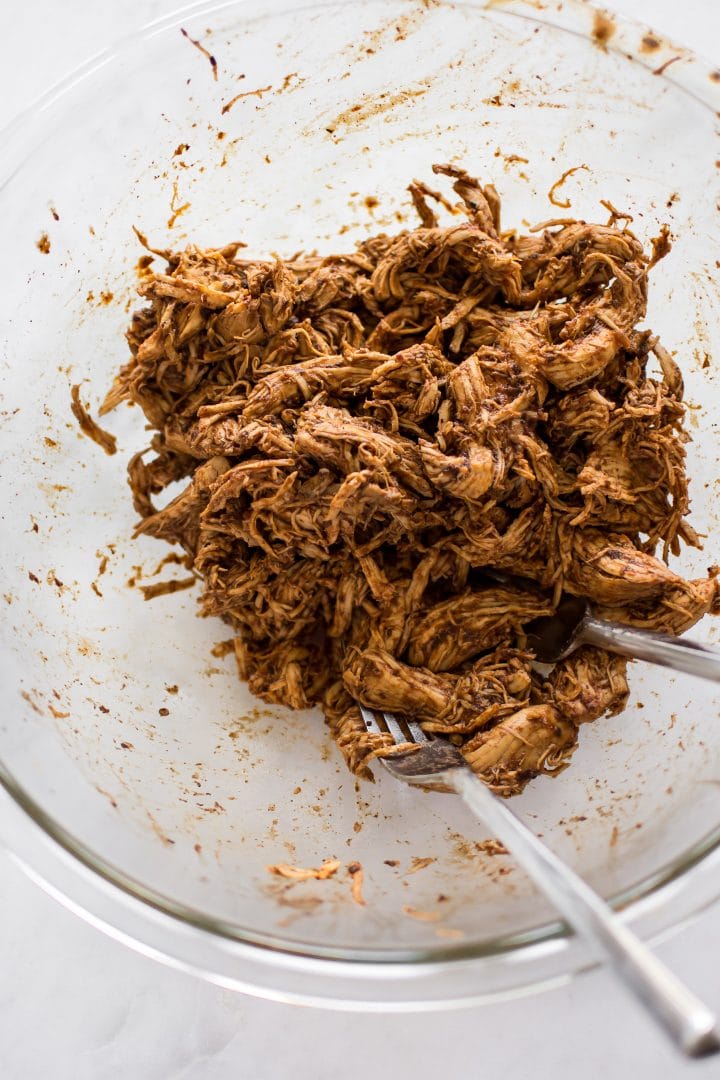 glass mixing bowl with shredded BBQ chicken and two forks