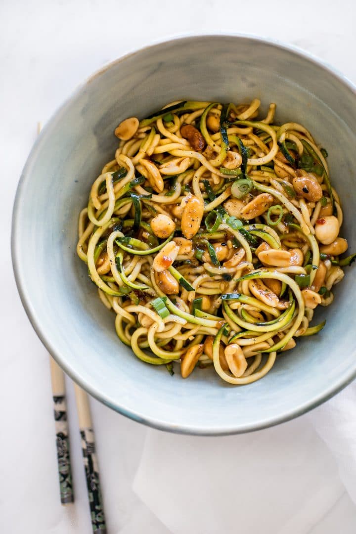 kung pao zucchini noodles with peanuts in a teal bowl with chopsticks