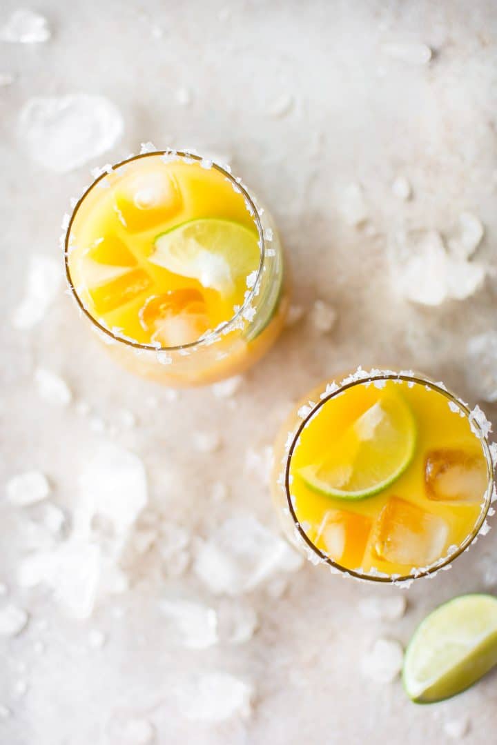 two glasses of mango margaritas with lime wedges and ice
