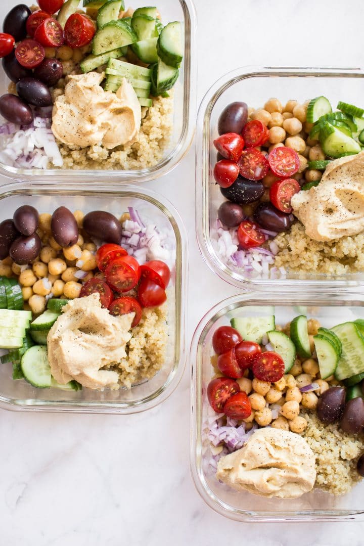 close-up of four glass meal prep glass bowls with Mediterranean quinoa, hummus, and vegetables