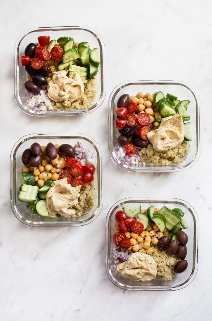 four Mediterranean vegan meal prep bowls with quinoa, chickpeas, hummus, olives, tomatoes, and cucumber