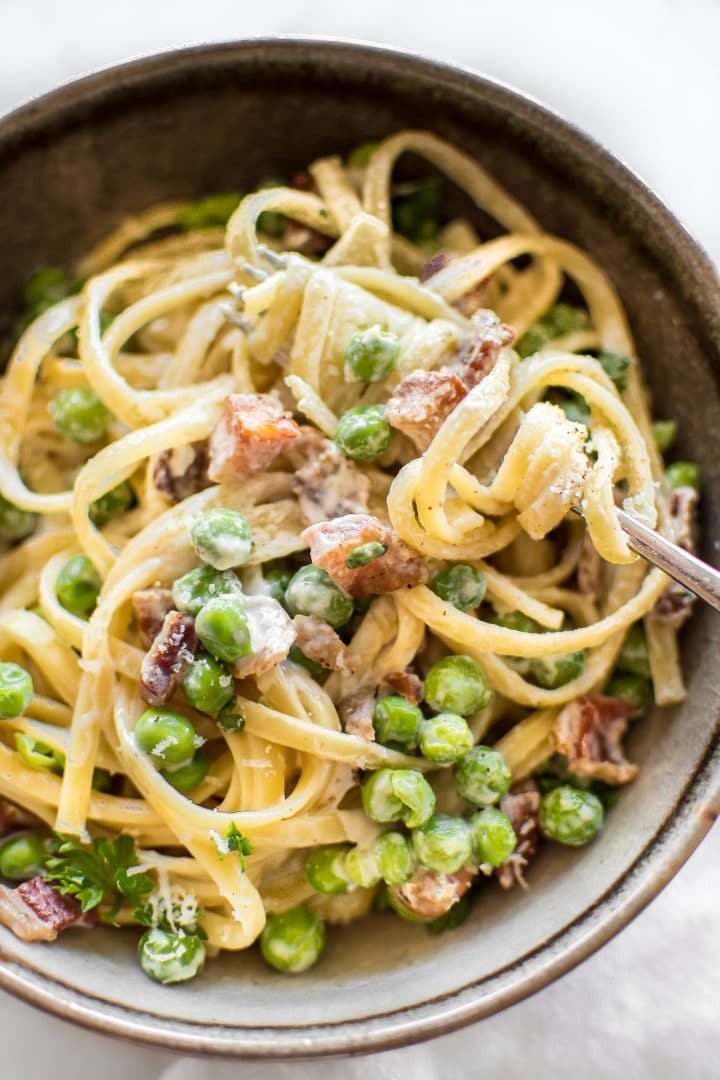 close-up of pasta with pancetta, peas, a creamy garlic sauce, and plenty of fresh parmesan and a fork
