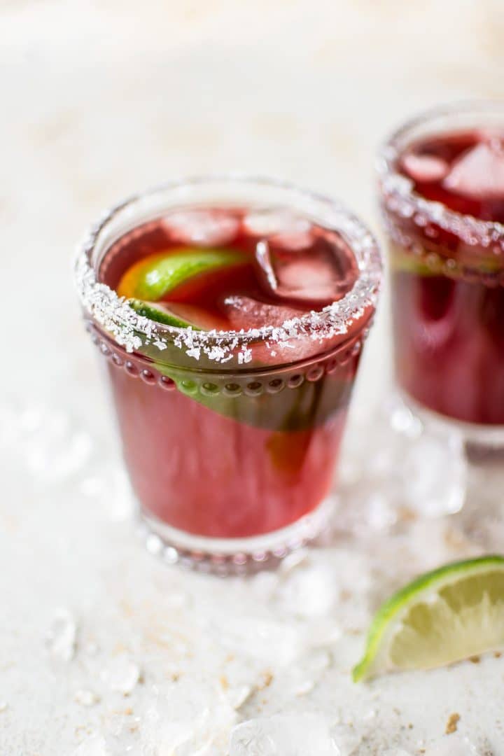 two pomegranate margaritas in glasses with ice and lime wedges